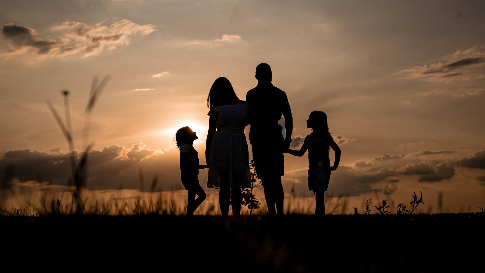 Silhouette of two parents and two children standing together in a field at sunset